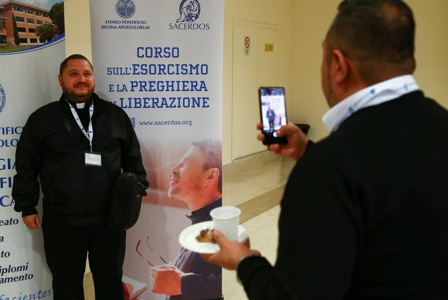 A priest poses for a picture next to a banner advertising a course for aspiring exorcists in Rome