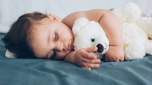 Beautiful baby sleeping with his teddy bear aside, family concep