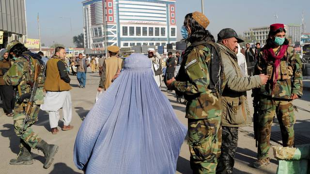 An Afghan woman wearing burqa walks past Taliban fighter Bader at the market in Kabul