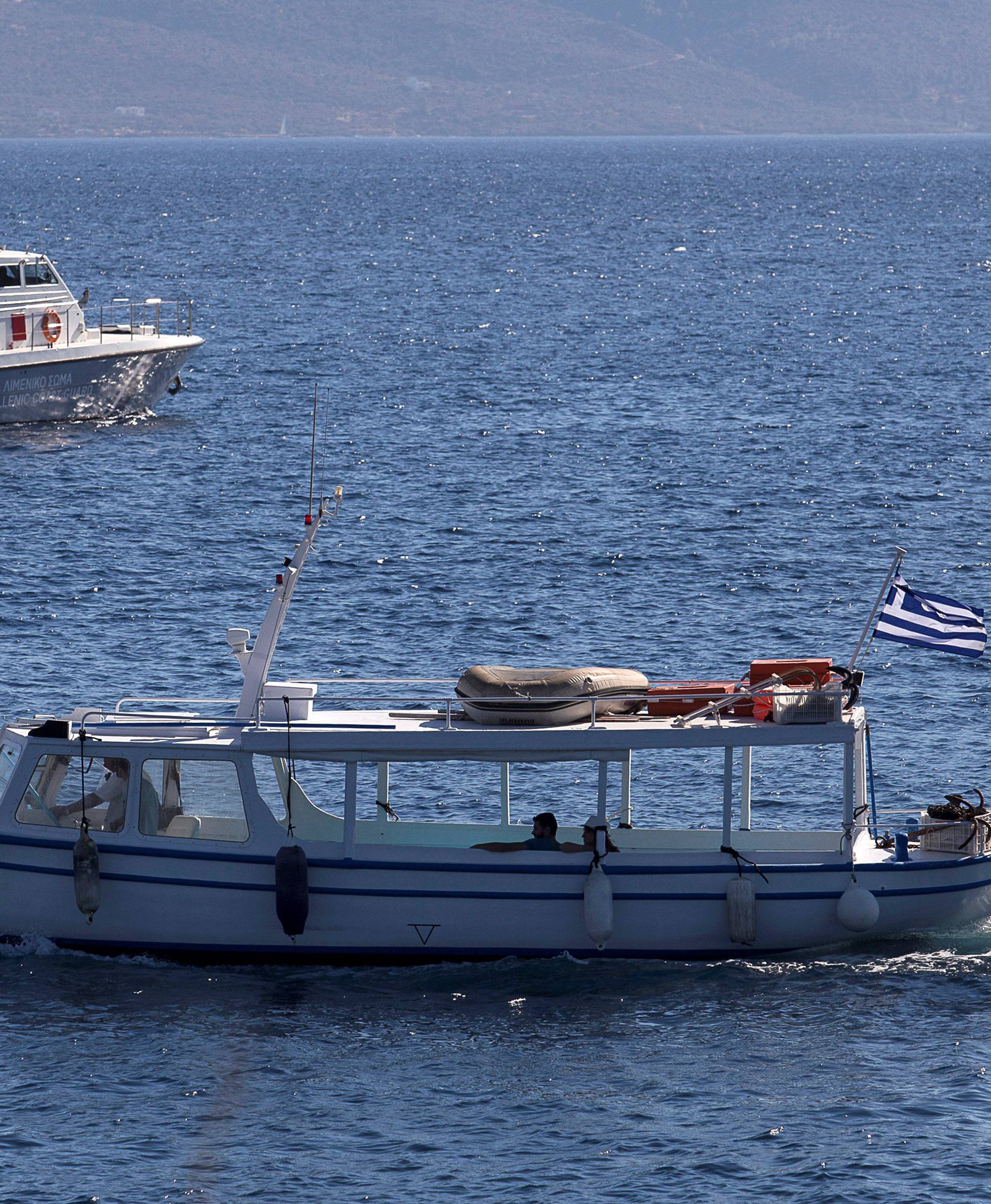 A coastguard boat inspect the area where four people, including a nine-year-old girl, died and at least five were injured after a boat with about 20 people on board collided with a speedboat off the Greek holiday island of Aegina close to Athens