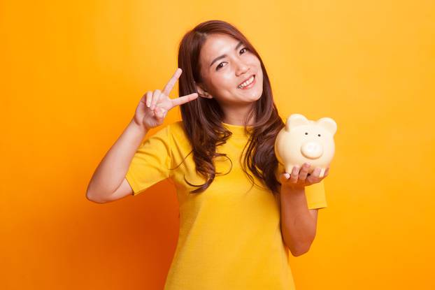Asian woman show victory sign with pig coin bank.