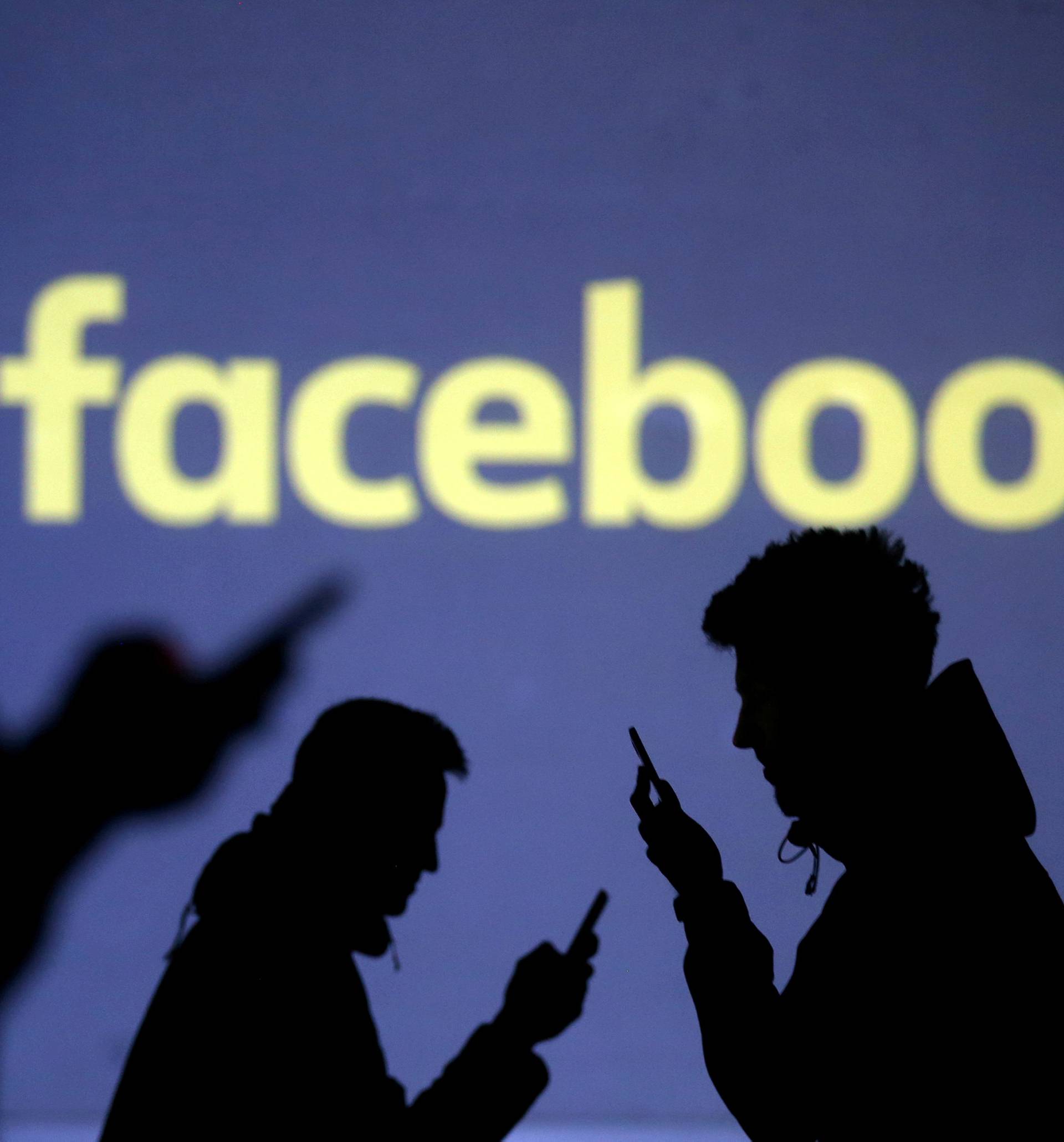 FILE PHOTO: Silhouettes of mobile users are seen next to a screen projection of Facebook logo in this picture illustration