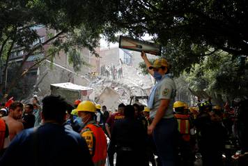 A woman holds up a tool for rescue workers who are searching for people under the rubble of a collapsed building after an earthquake hit Mexico City