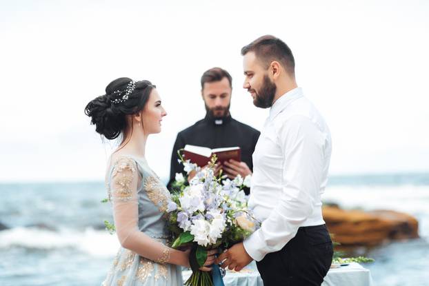 wedding couple on the ocean with a priest