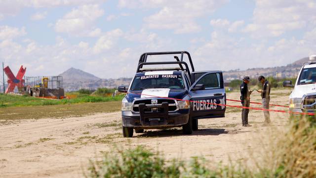Police and forensic technicians stand near the body of an alleged migrant on the banks of the Rio Bravo river in Ciudad Juarez