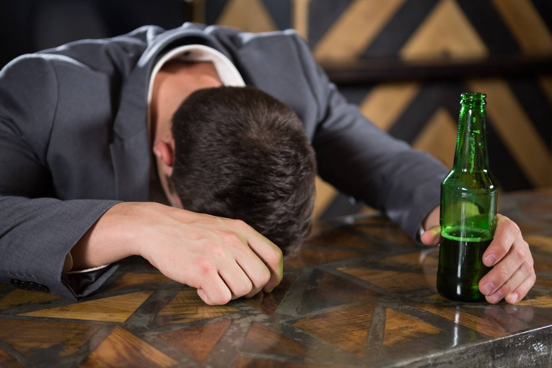 Drunk man lying on a counter with bottle of beer