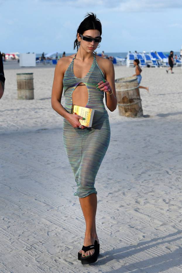 Singer Dua Lipa wears a black string bikini under a sheer knit coverup a she hits the beach in Miami