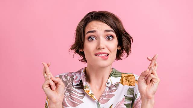 Photo of young girl bite lips teeth crossed fingers worried hope luck success isolated over pink color background