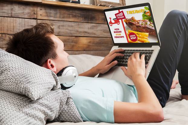 Man ordering take away food by internet with a laptop while lyin