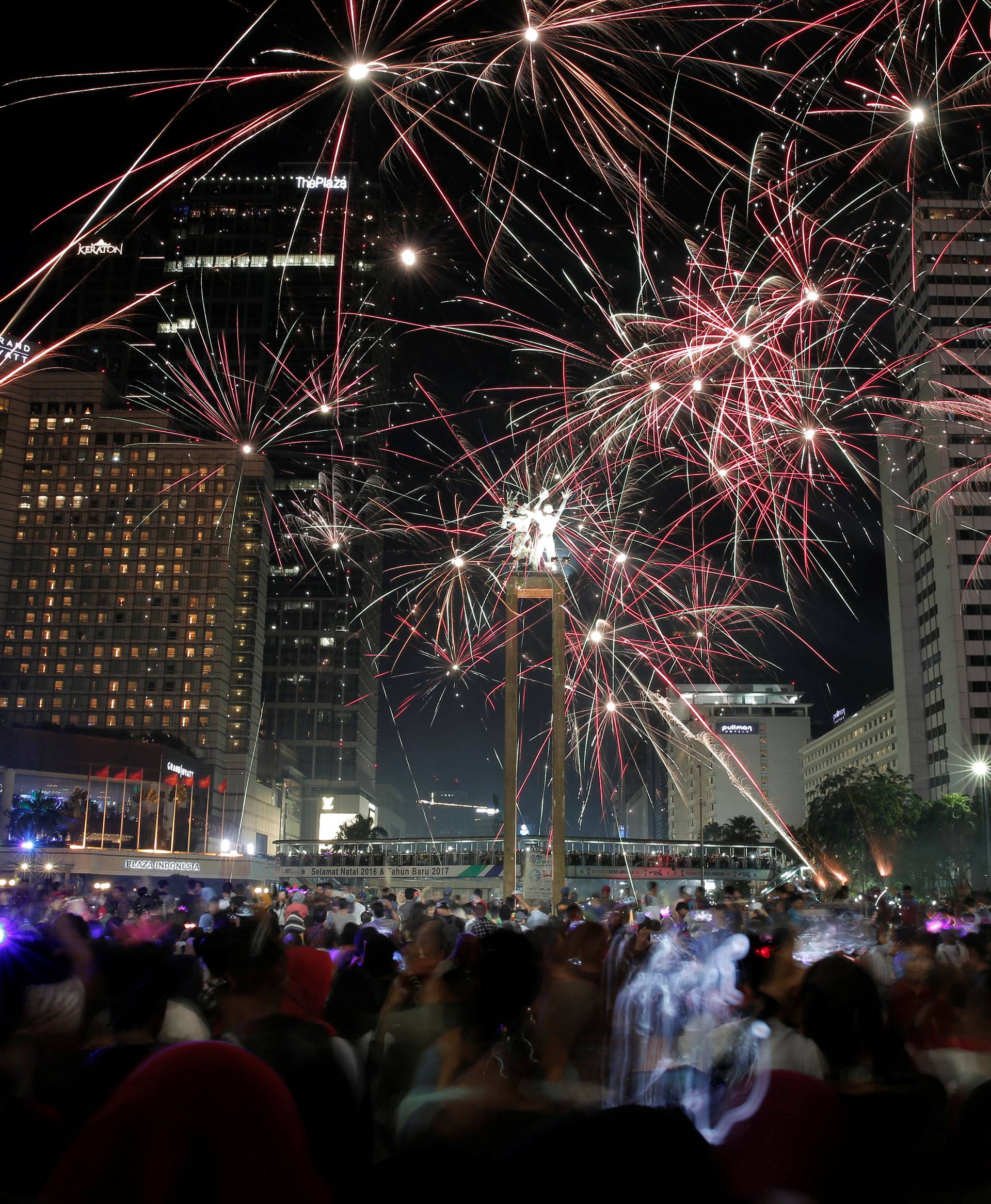 People watch fireworks explode around the Selamat Datang Monument during New Year's Eve celebrations in Jakarta