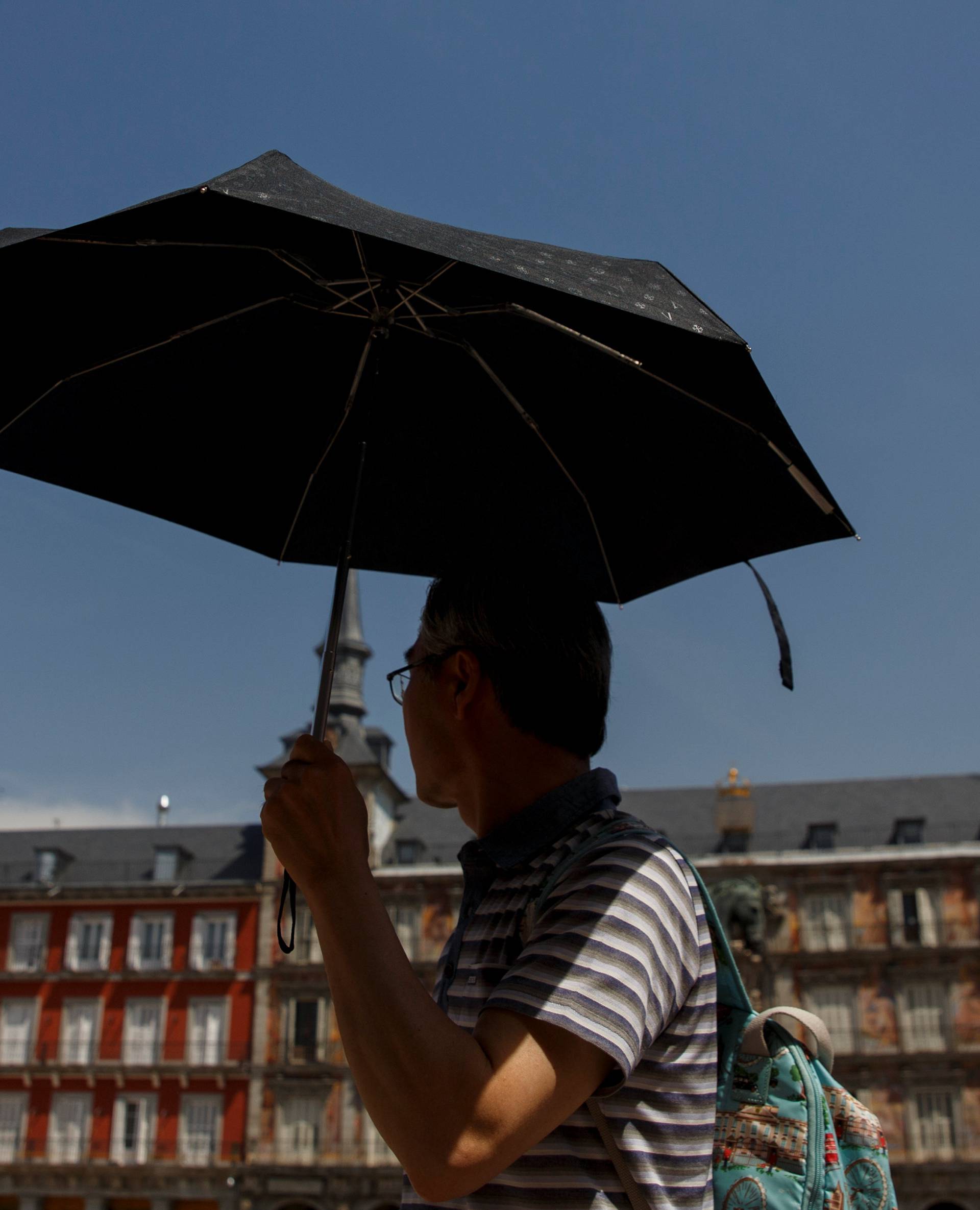 A tourist uses an umbrella to shield himself during a heatwave at Plaza Mayor in Madrid