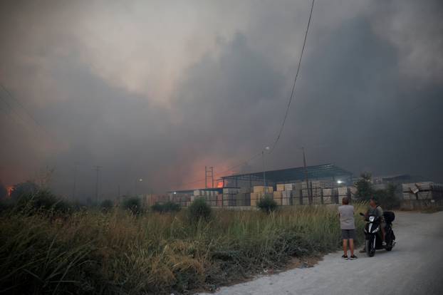 People watch a fire at a cement factory sparked by a nearby wildfire, in Patras