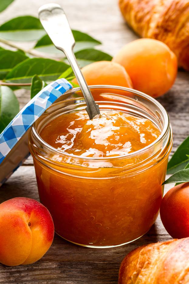 Tasty fruit orange apricot jam in glass jar with fruits on wooden table. Closeup.