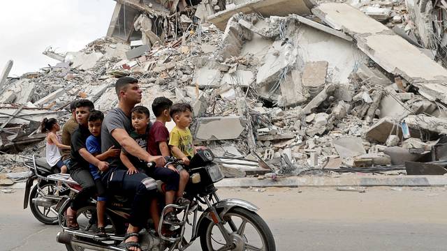 Palestinians ride a motorcycle past the site of an Israeli air strike in Gaza