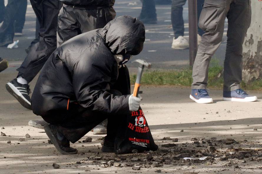 A masked and hooded protester uses a hammer to gather rocks during clashes with French CRS riot police at the May Day labour union rally in Paris
