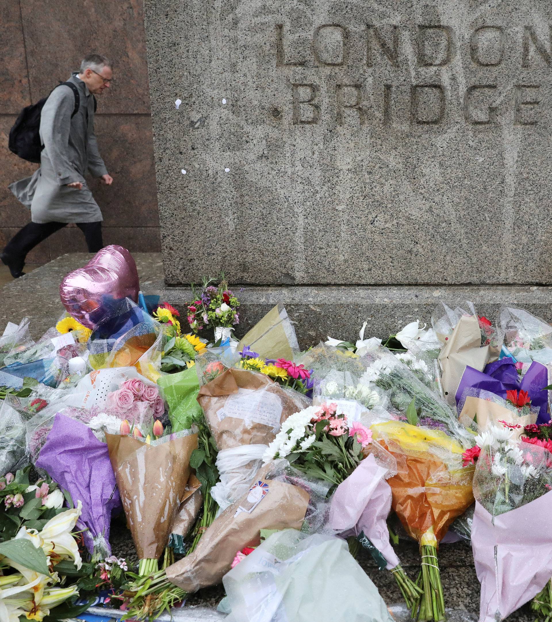 FILE PHOTO: A man walks past flowers and tributes left for the victims of the attack on London Bridge and Borough Market on a wet and windy morning in London