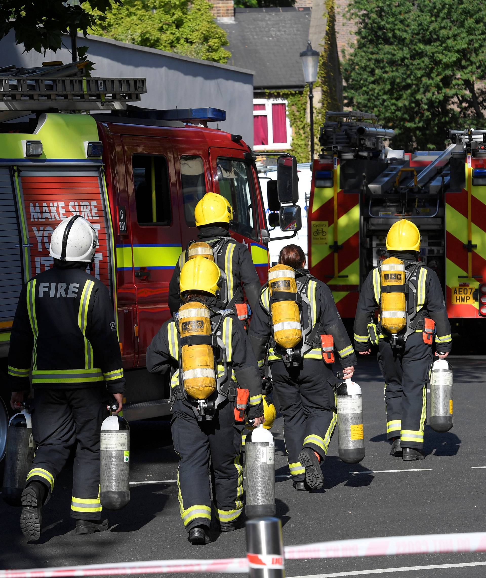 Firefighters carry gas cylinders near a tower block severly damaged by a serious fire, in north Kensington, West London