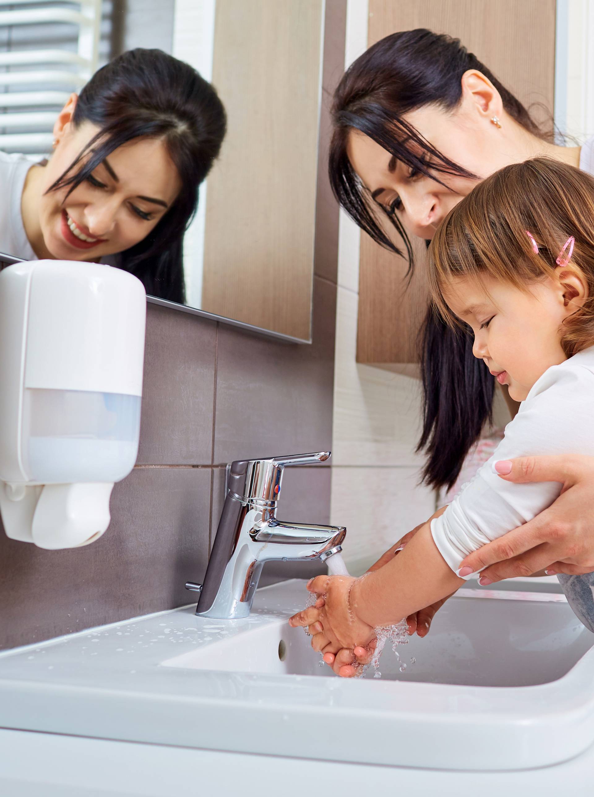 Kid washing hands with mom in the bathroom.