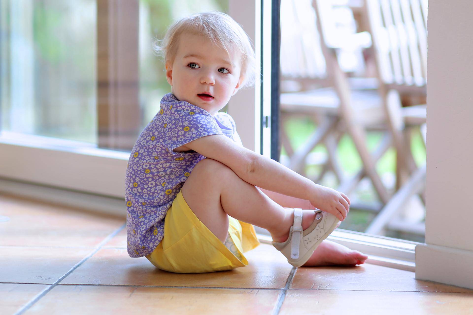 Toddler girl putting shoes sitting on floor next to window