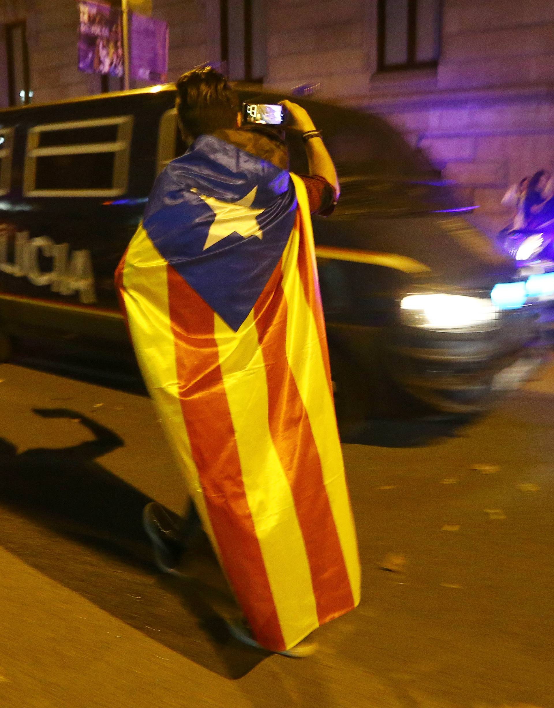 A man wearing a separatist Catalan flag films officers of the Spanish National Police outside the High Court of Justice of Catalonia in Barcelona