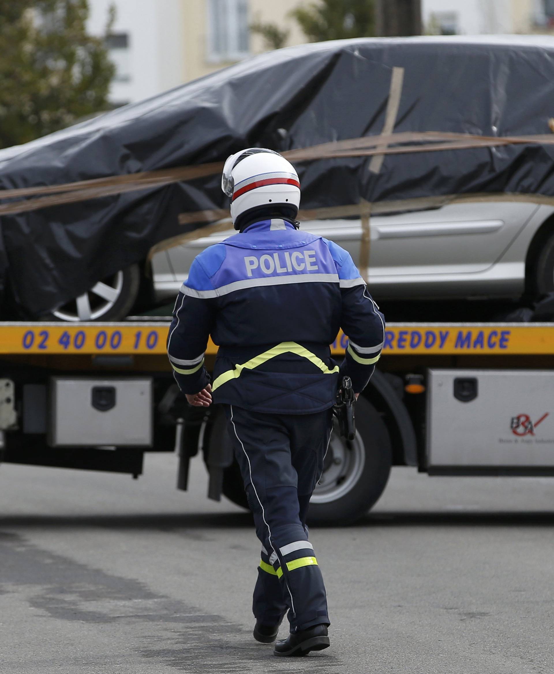 A French policeman walks towards the covered abandoned automobile of Sebastien Troadec in a parking lot in Saint Nazaire