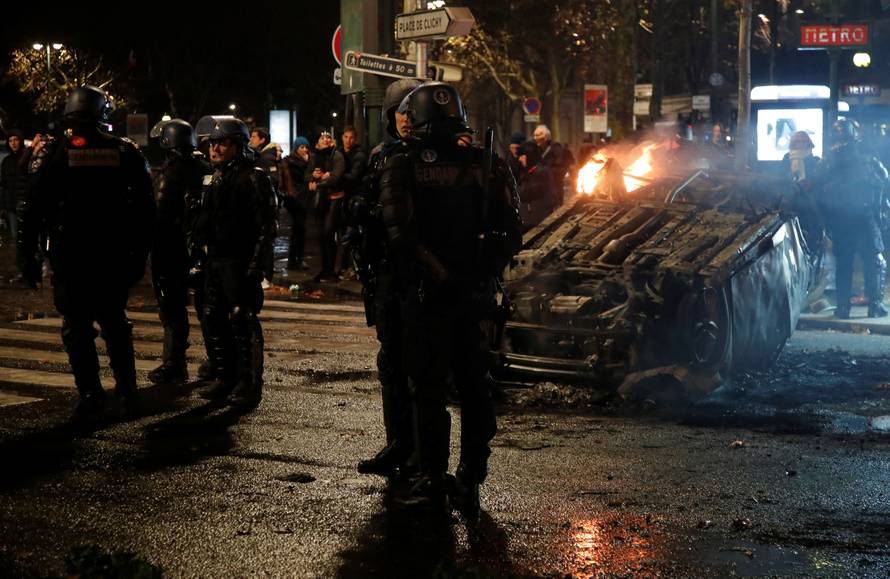 French riot police stand near an overturned burning car on avenue Kleber after clashes with protesters wearing yellow vests, a symbol of a French drivers' protest against higher diesel taxes, in Paris
