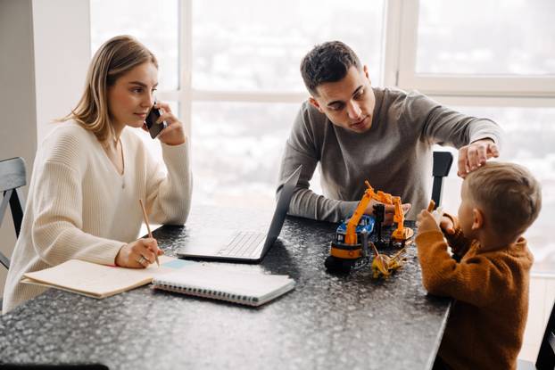 Young woman working on laptop while man playing with son over table
