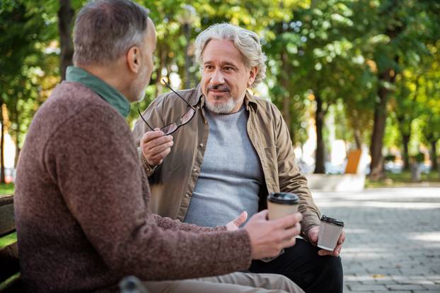 Joyful senior male friends enjoying hot beverage outdoor