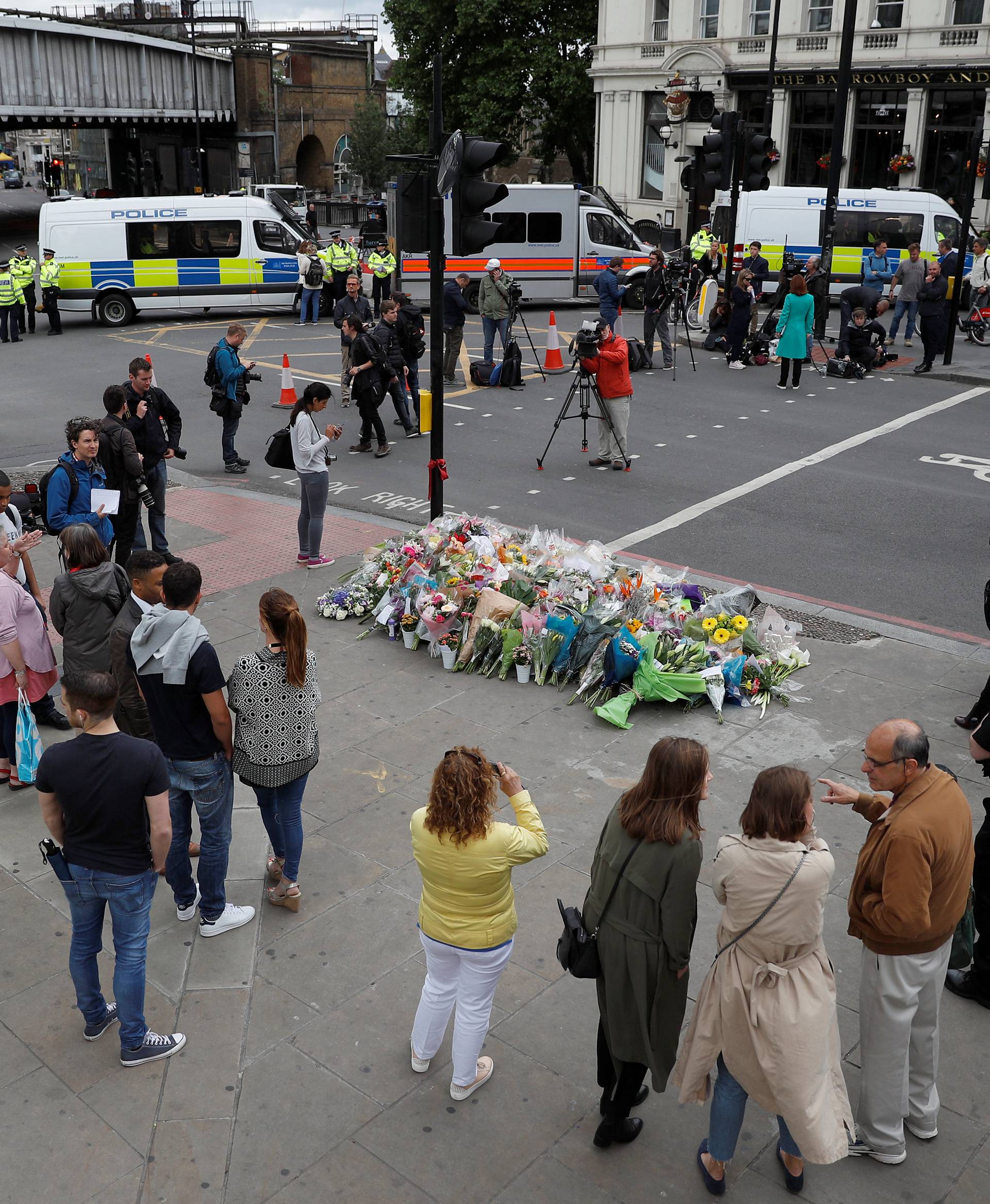 People stand around floral tributes on the south side of London Bridge near Borough Market after an attack left 7 people dead and dozens of injured in London