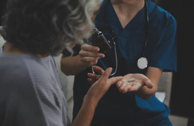 Female caregiver doing regular check-up of senior woman in her h