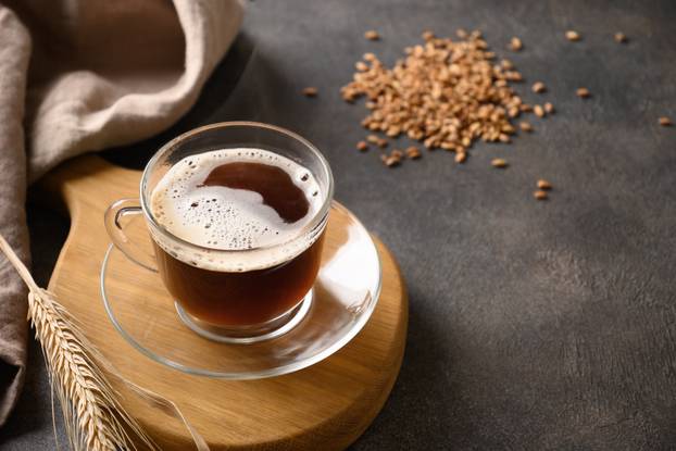 Barley coffee in white cup and ears of barley on brown background.