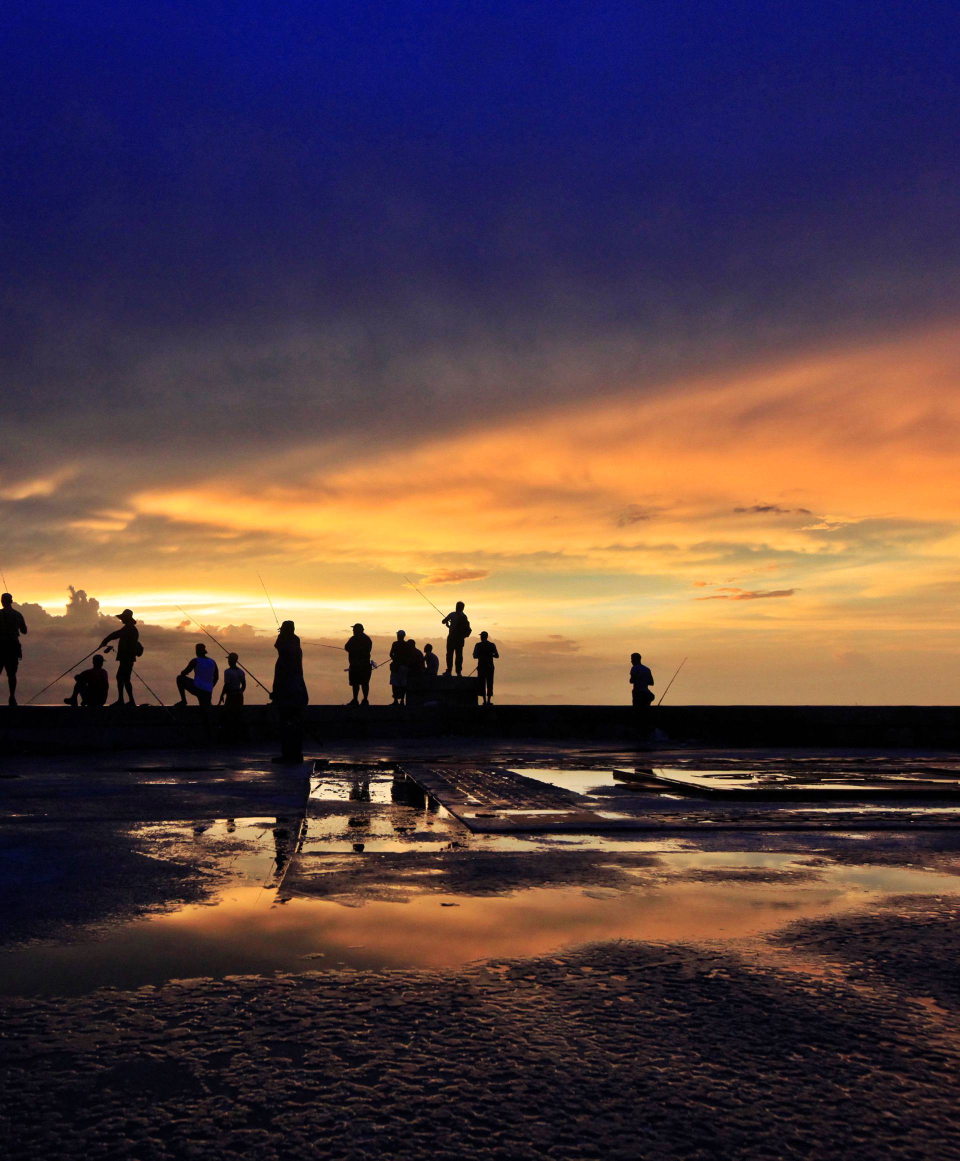 Fishermen stand along Havana's seafront boulevard 'El Malecon' during sunset 