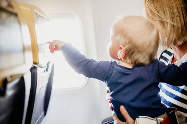 Mom and child flying by plane. Mother holding and playing with her infant baby boy child in her lap during economy comercial flight. Concept photo of air travel with baby. Real people.
