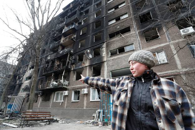 A local resident points at a damaged apartment building in the besieged city of Mariupol