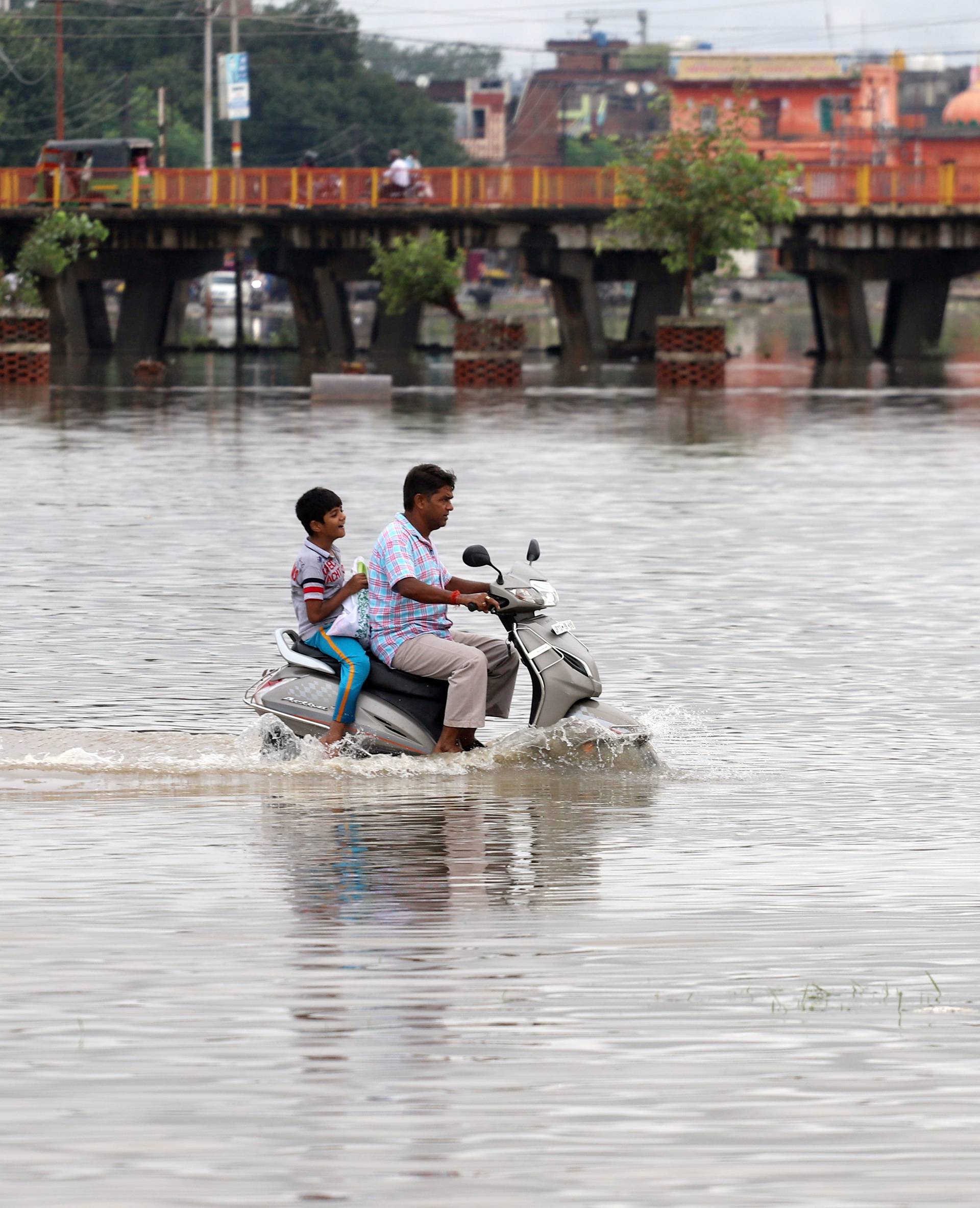 A man and a boy ride a scooter through a flooded road after heavy rains in Prayagraj