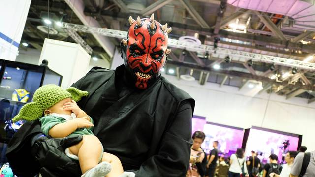 A cosplayer dressed as Darth Maul from Star Wars, carrying a child dressed in a Yoda hat, poses during the Singapore Comic Con, in Singapore