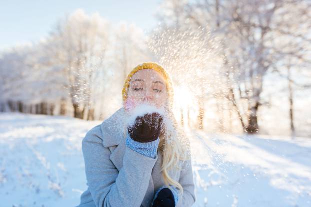 Winter girl blowing snow in frosty winter park, young woman having fun in winter park. Sunset shot with selective focus