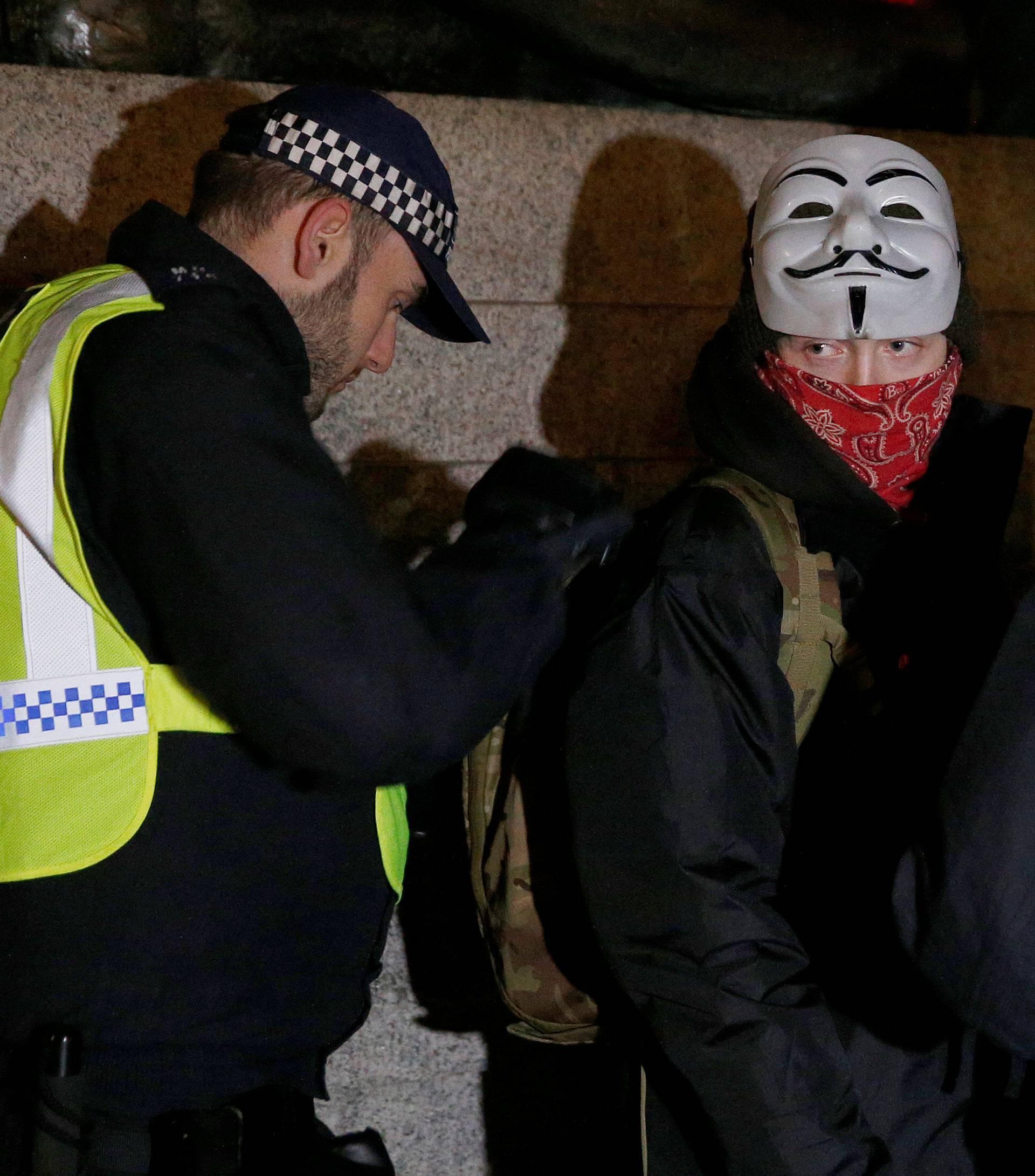 Police officers search a protester during the "Million Mask March" in London