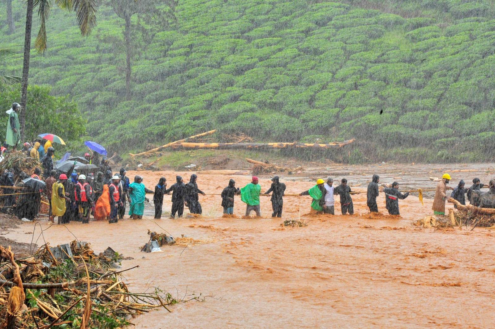 Rescuers help people to cross a flooded area after a landslide caused by torrential monsoon rains in Meppadi in Wayanad