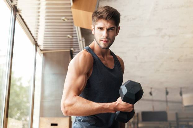 Fitness man stands sideways in gym