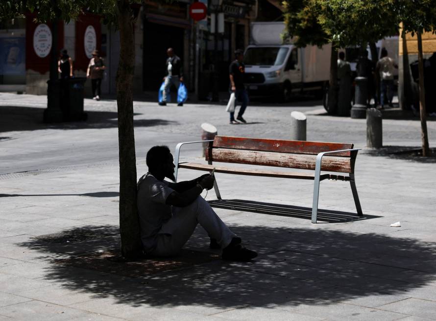 A man sits in the shade of a tree to escape the heat during a heatwave in Madrid, Spain