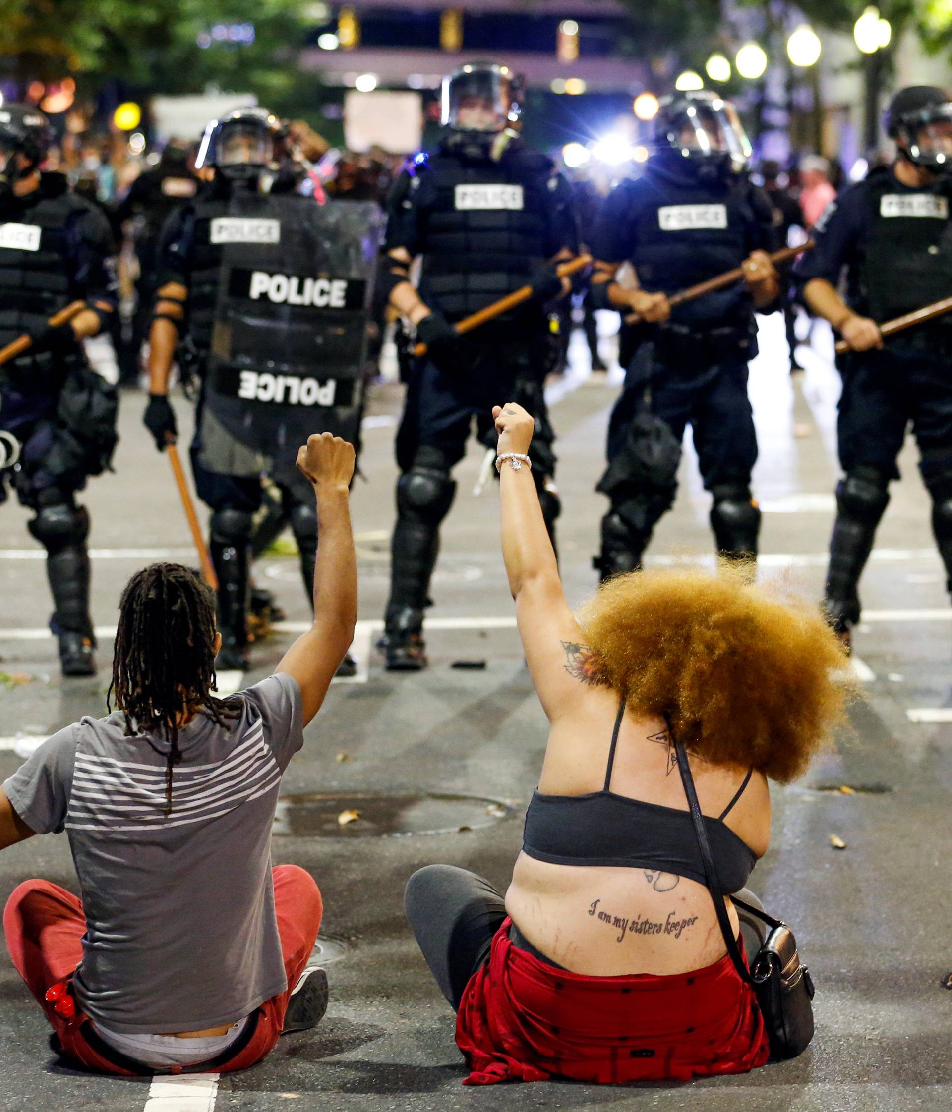 Two people sit on the ground as they protest in front of police in uptown Charlotte, NC  during a protest of the police shooting of Keith Scott, in Charlotte