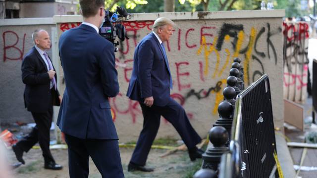 U.S. President Trump walks past a building defaced with graffiti by protestors in Washington