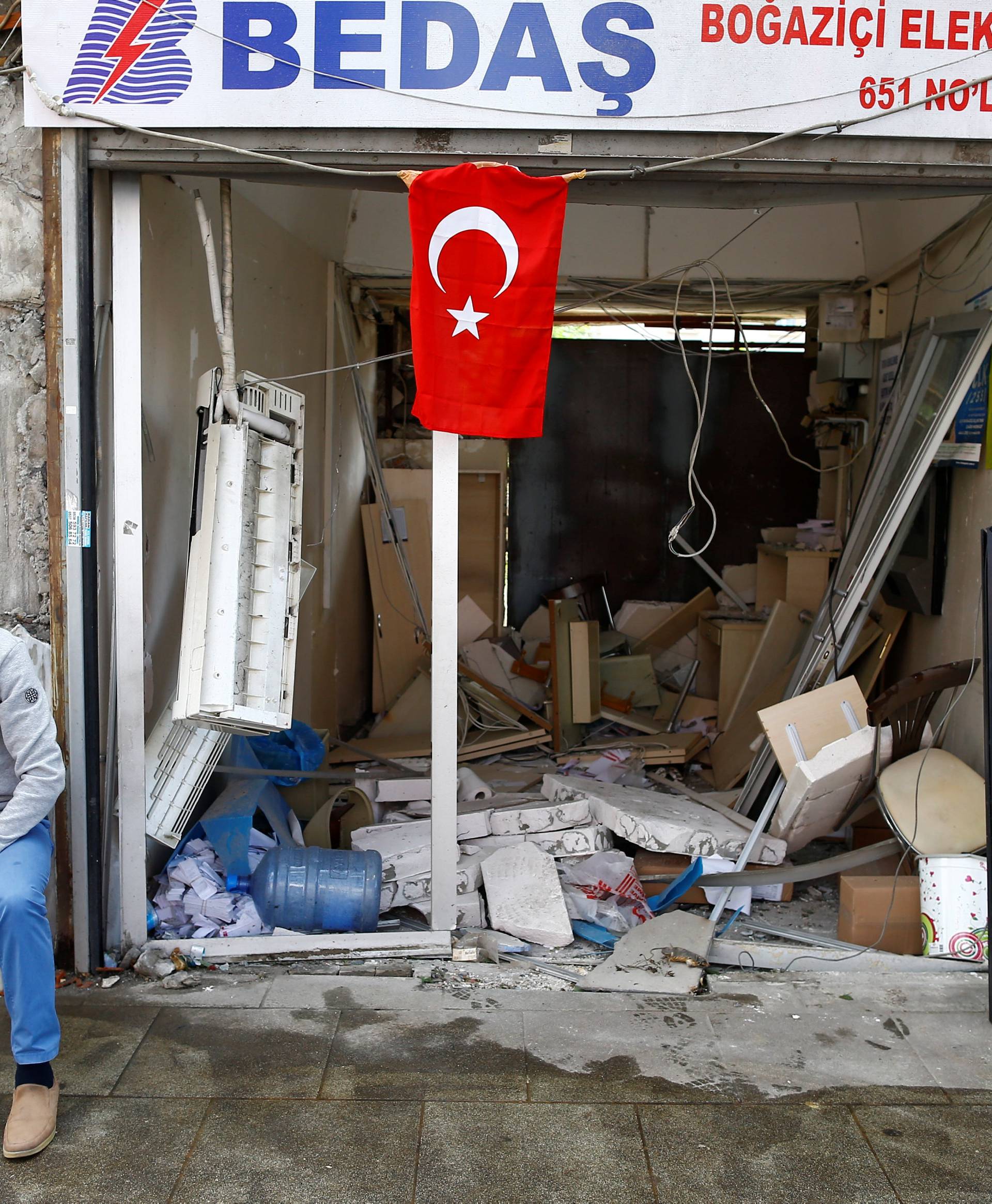 A man sits in front of a damaged shop near the scene of Tuesday's car bomb attack on a police bus, in Istanbul