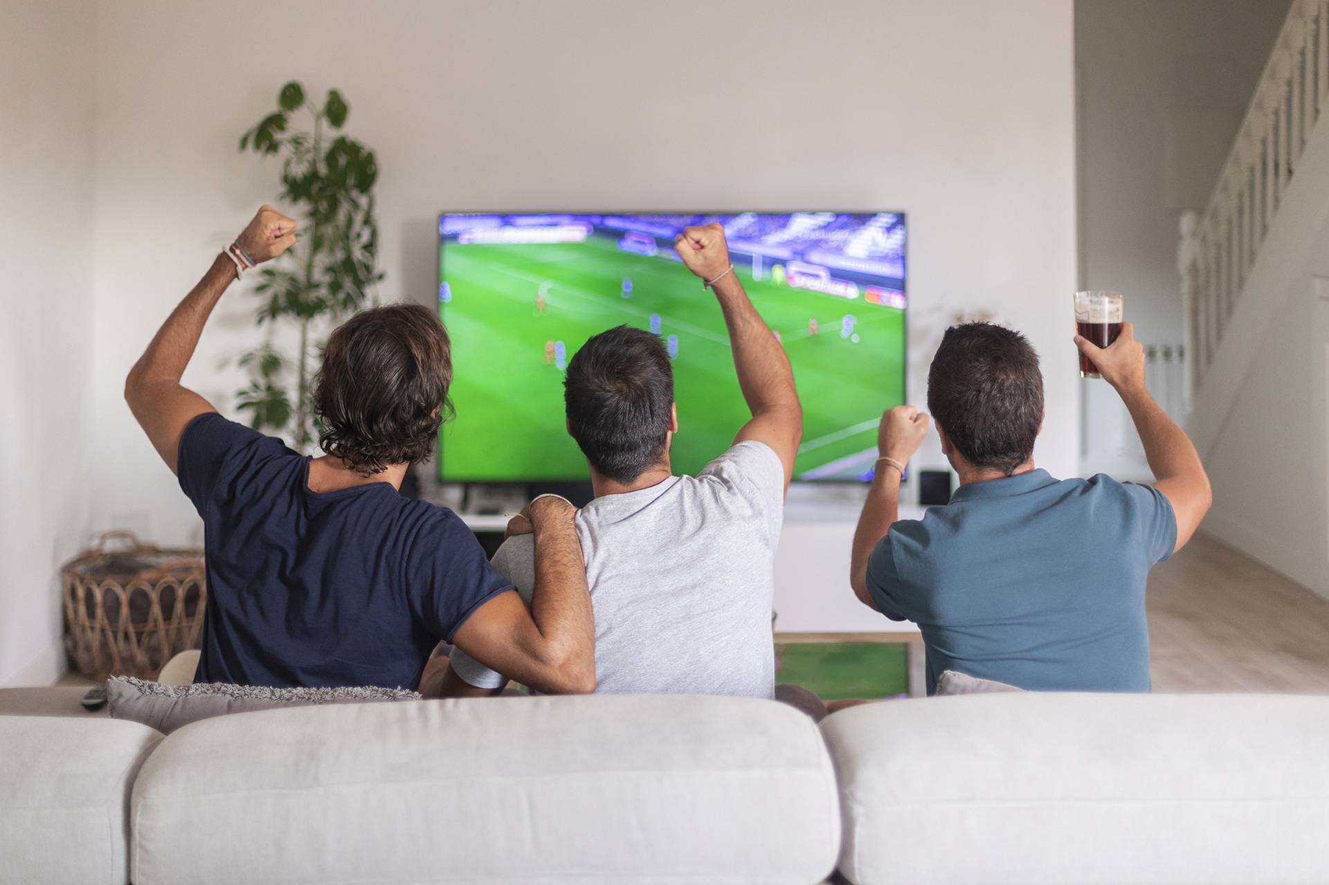 Three friends watching a soccer game at home drinking beer