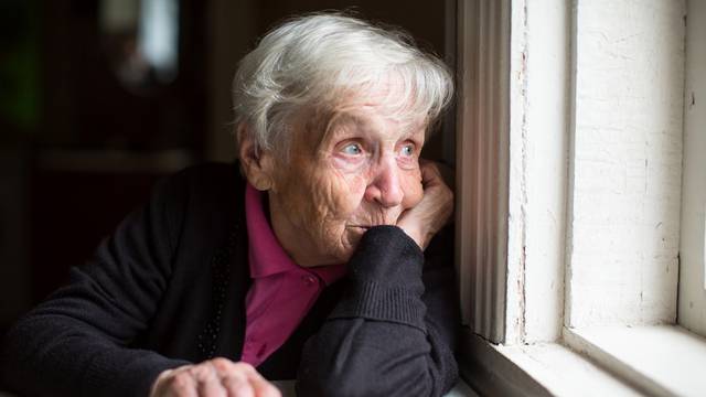 An,Elderly,Woman,Looks,Sadly,Out,The,Window.