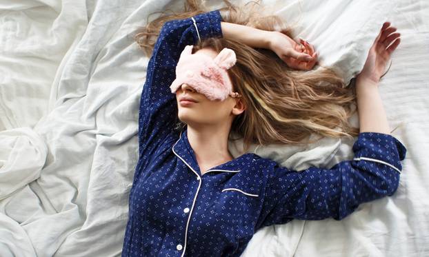 Cute blonde in her bed in blue pajamas and sleep mask, top view