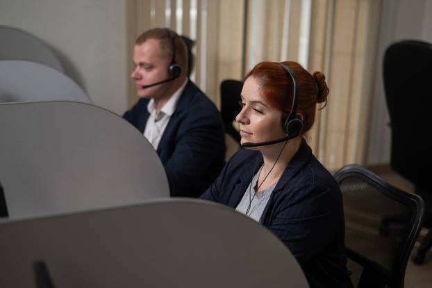 Two serious call center employees are talking with clients. Man and woman working with headsets in office. 