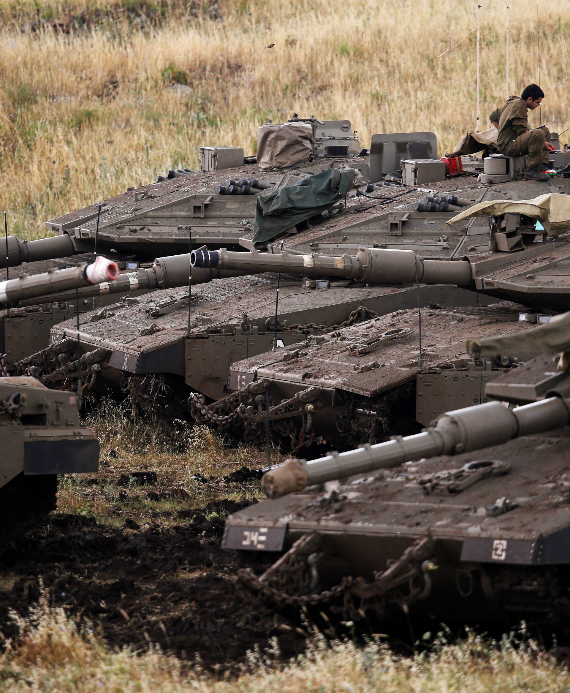 Israeli soldiers sit on tanks near the Israeli side of the border with Syria in the Israeli-occupied Golan Heights
