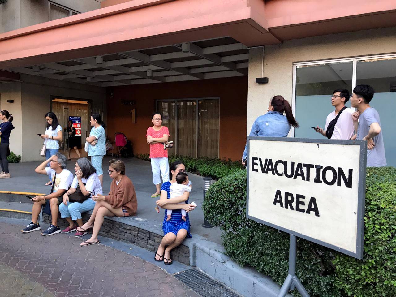 Residents sit outside after being evacuated from the condominium building after an earthquake in Makati City
